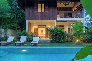 A two-story house with a pool, lounge chairs, and a well-maintained garden.