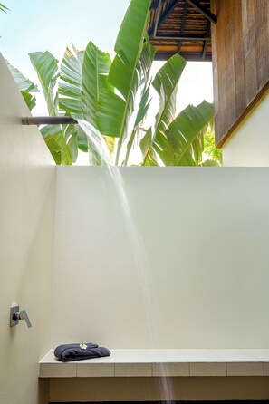 A bathroom with a shower, a towel, and a view of banana leaves.