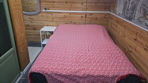 Una habitación pequeña de madera con una cama, un reloj de pared y una pintura de Buda.