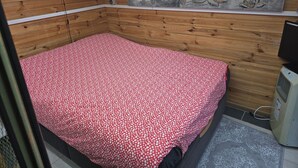 Habitación de cabaña de madera con cama, un reloj, una pintura de Buda y un calefactor.