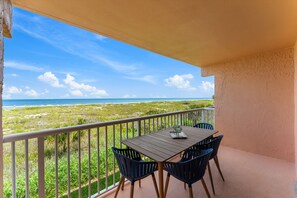 A balcony with a table and chairs, overlooking a beach and ocean. - Stunning Oceanfront Condo W/ Private Balcony & Heated Pool! 🌊 (Cocoa Beach)