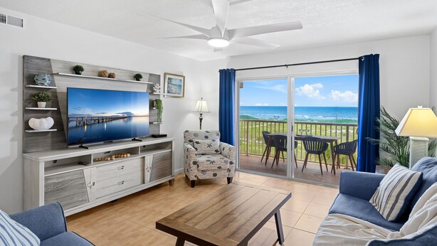 Ein Wohnzimmer mit Fernseher, Sofa, Couchtisch und einem Balkon mit Meerblick.