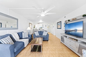 Ein modernes Wohnzimmer mit Sofa, Couchtisch, Fernseher und Deckenventilator.