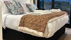 Une chambre à coucher moderne avec un grand lit, de nombreux oreillers, une couverture et une vue sur l’extérieur grâce à une grande fenêtre.