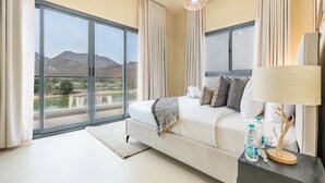 A bedroom with a large bed, a nightstand with a lamp, and a view of mountains through large windows.