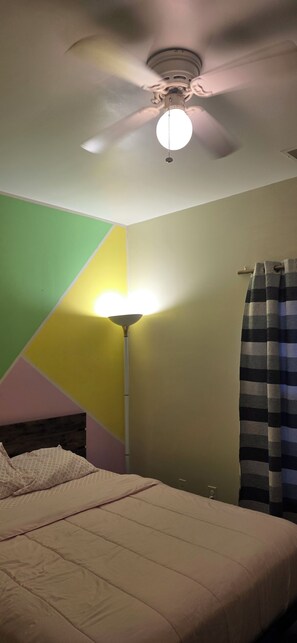 Un dormitorio con una cama, un ventilador de techo y una lámpara de pie.