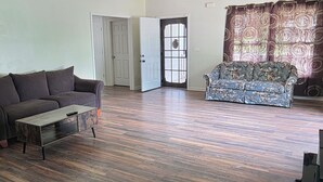 A living room with a brown sofa, a wooden coffee table, and a patterned sofa. There are two doors, one open and one closed. - 3 BR house (sleeps 8 adults) 8 minutes from Atlanta stadium & downtown (Atlanta)