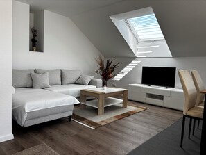 Ein modernes Wohnzimmer mit einer Couch, einem Couchtisch, einem Fernseher und einem Oberlicht.