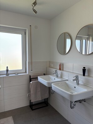 Een moderne badkamer met twee wastafels, een raam en twee spiegels aan de muur.