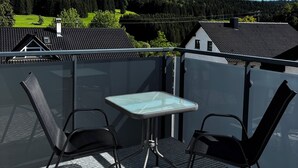 Un balcone con un tavolo in vetro e due sedie, affacciato su un pendio boscoso.