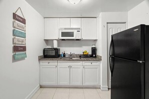 Eine Küche mit weißen Schränken, einer Mikrowelle, einem Toaster, einer Kaffeemaschine und einem Kühlschrank.