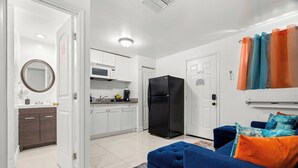 A modern kitchen with white cabinets, a black refrigerator, and a microwave. There is a blue sofa with orange and blue cushions. - Cozy Apt, King Bed + Huge TV, Near TPA & Stadium (Tampa)