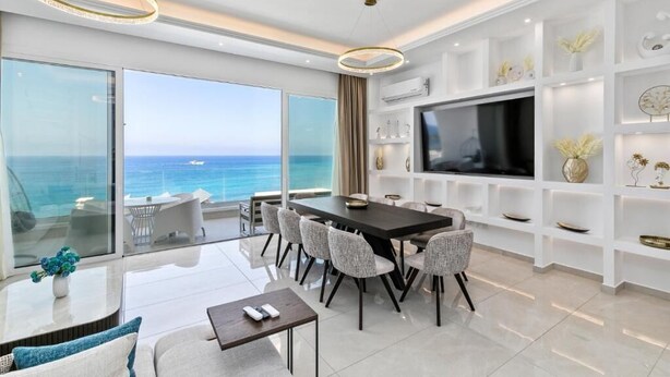 Ein modernes Wohnzimmer mit großem Fernseher, Essbereich und einem Balkon mit Meerblick.