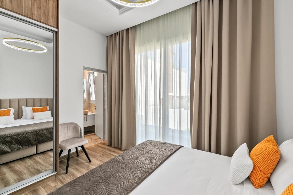 A modern hotel room with a bed, a chair, a desk, and a large window with curtains.