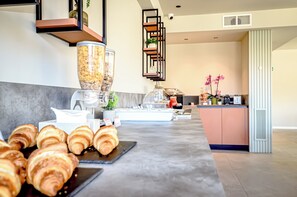 A breakfast bar with pastries, a coffee machine, and a decorative shelf with plants. - CP Hotels-Central (Milan)