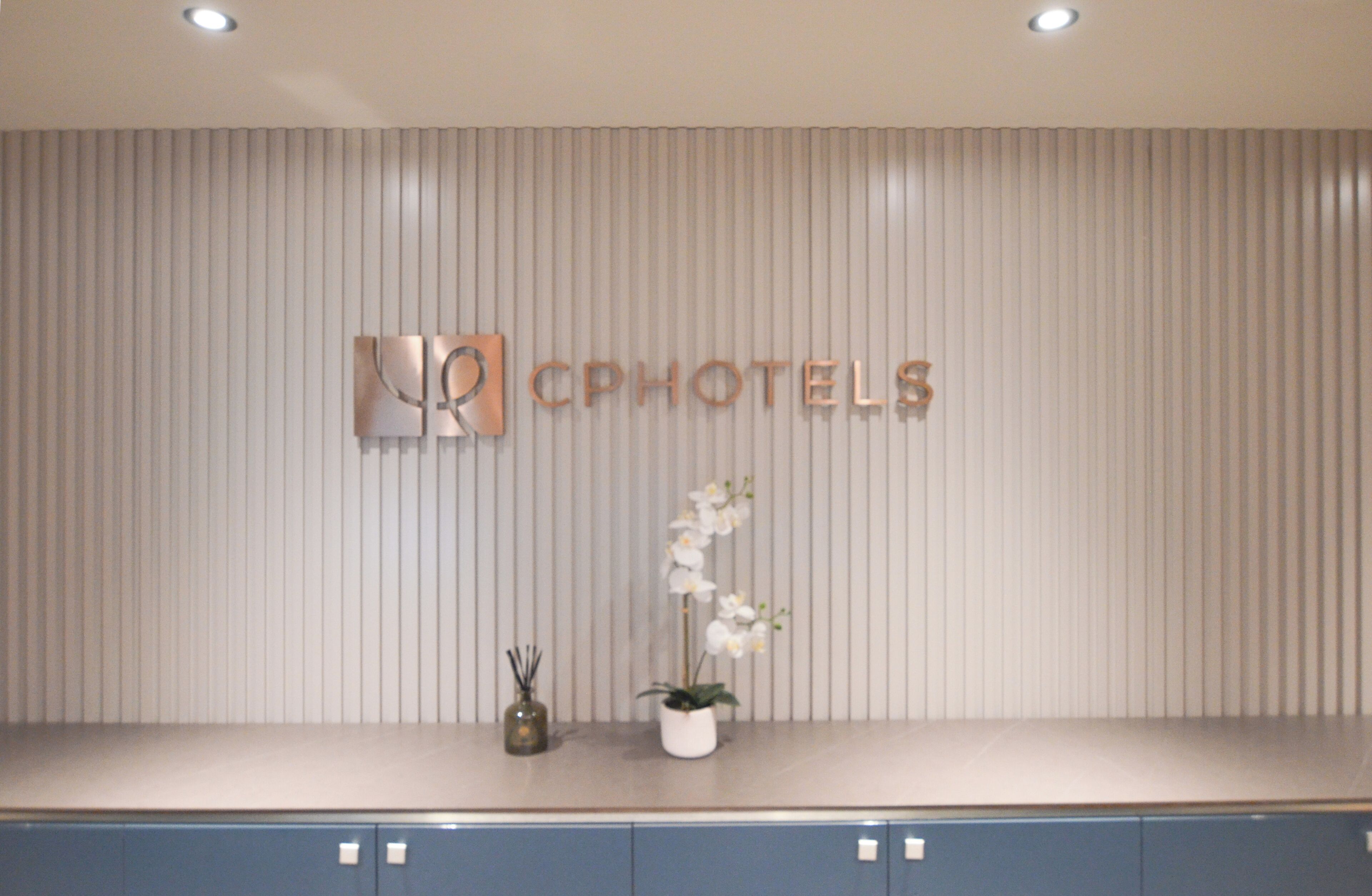A reception desk with a vertical striped wall, a logo, and a potted orchid.