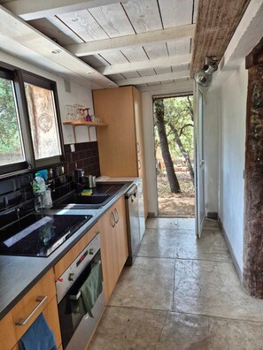 Une cuisine dotée d’un plan de travail noir, de meubles en bois, d’un four encastré et offrant une vue sur un espace extérieur grâce à une porte ouverte.