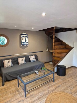 Une pièce comprenant un canapé, une table basse, un escalier en bois, une horloge murale et un tableau encadré.