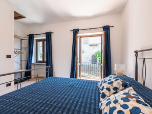 A bedroom with a bed, a window with curtains, a radiator, and a view of a courtyard. - Vacation home Velina by Interhome (Alba)