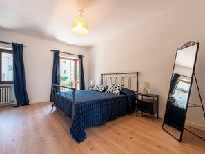 Ein Schlafzimmer mit einem Bett, einem Nachttisch, einem Spiegel und einem Fenster mit Vorhängen.