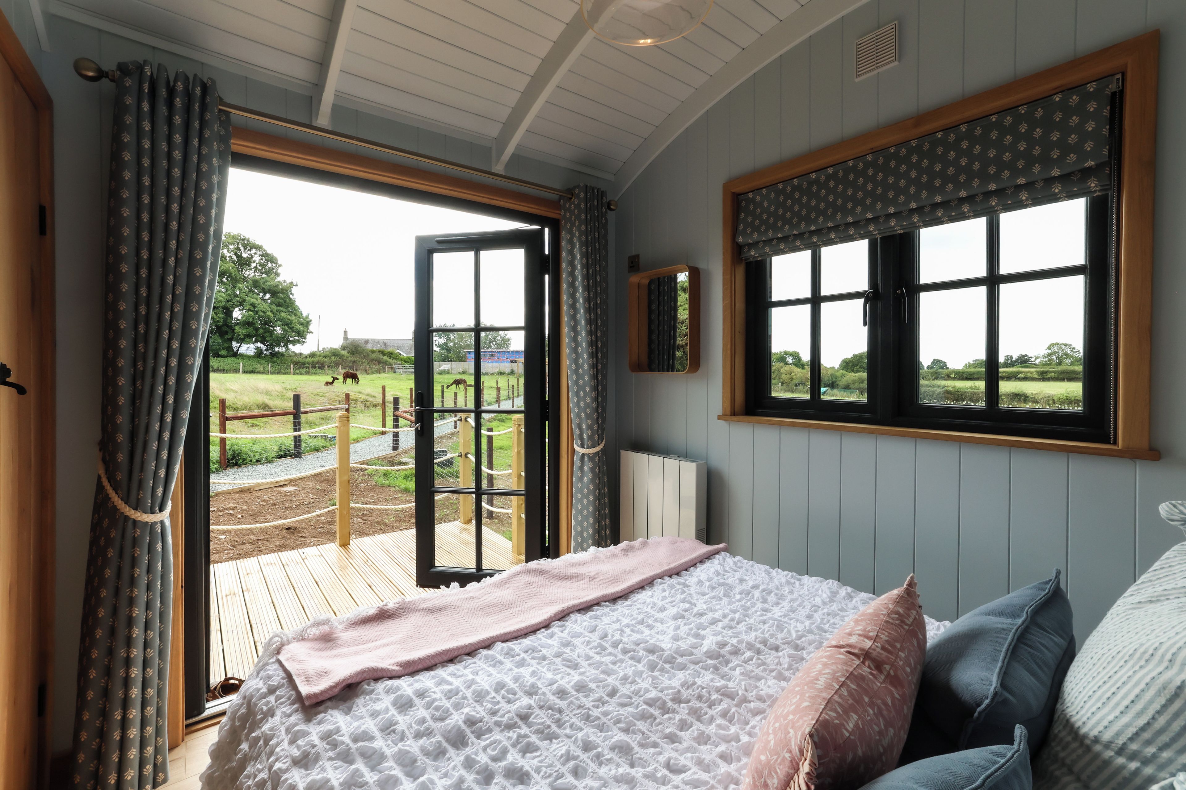 A bedroom with a large bed, a window with a view of a fenced outdoor area, and a radiator.