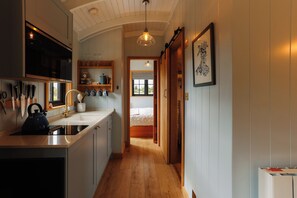 A kitchen with a sink, kettle, and utensils, leading to a bedroom with a window. - Luxury Shepherds Hut with hot tub, firepit and gas barbeque (Anglesey)