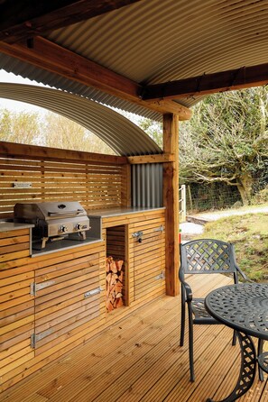 An outdoor wooden deck with a grill and seating area. - Luxury Shepherds Hut with hot tub, firepit and gas barbeque (Anglesey)