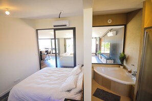 Une chambre d’hôtel avec un lit, une salle de bain avec une baignoire et un grand miroir.