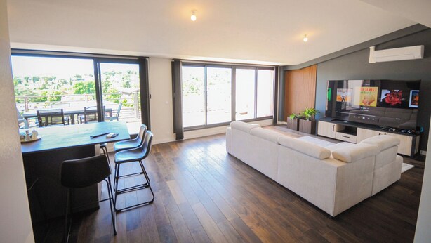 Ein modernes Wohnzimmer mit Sofa, Fernseher und Essbereich mit Stühlen und Tisch.