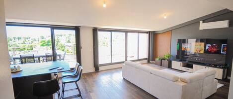 A modern living room with a sofa, TV, and dining area with chairs and a table.