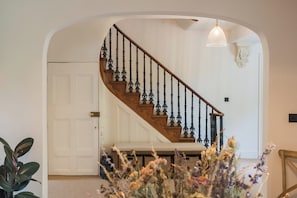 Eine Treppe mit Holzgeländer und schwarzen Spindeln, die zu einer Zwischenebene mit einer weißen Tür und einem Korb führt.