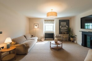 Ein Wohnzimmer mit einer Couch, einer Lampe, einem Tisch, einem Sessel, einer Heizung, einem Kamin und einem Fenster.