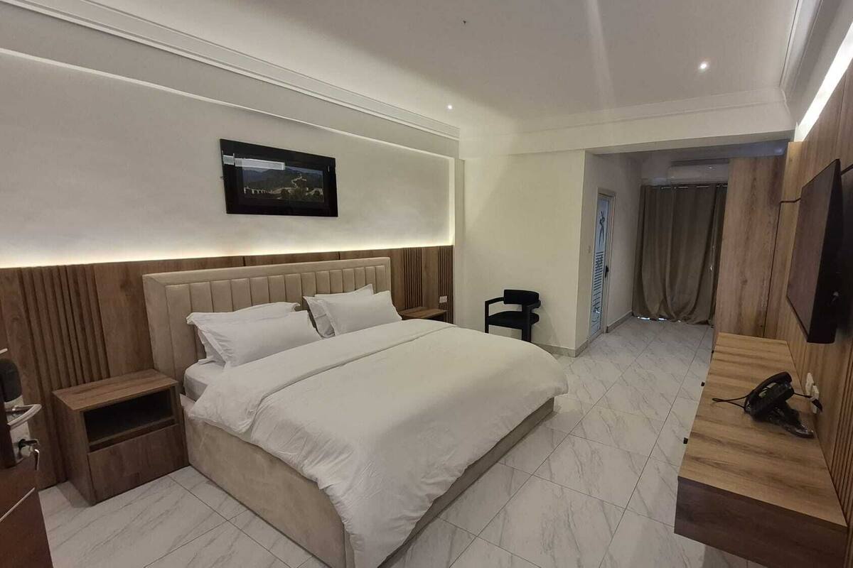 Une chambre à coucher moderne avec un grand lit, des tables de chevet, un téléviseur fixé au mur et un mur revêtu de panneaux en bois.