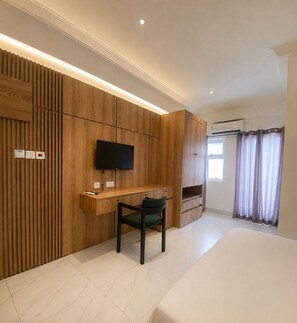 Un dormitorio moderno con cama, escritorio con silla, televisor montado en la pared y ventana con cortinas.