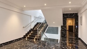 Un interior moderno con una escalera, piso de mármol y un ascensor de vidrio.