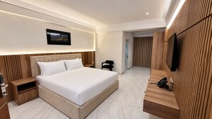 A modern hotel room with a large bed, bedside tables, a flat-screen TV, and a wooden panel wall. - Bruce Palace Hotel (Ngleshi Amanfro)