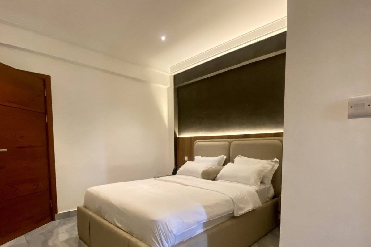 Une chambre moderne avec un grand lit, une porte en bois et un sol recouvert de carreaux de marbre.