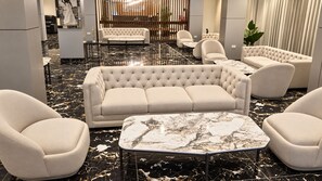Un interior moderno con un sofá capitonado, sillones y una mesa de centro de mármol.