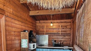Una baita di legno con tetto di paglia, un tavolo da pranzo, un angolo cottura con tovaglia blu e una piccola pianta verde.
