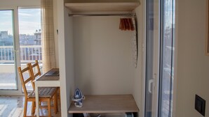 A room with a sliding glass door, a wooden table with an iron, a chair, and a small shelf. - Studio with a view of the Acropolis, close to the metro and tourist attractions (Athina)