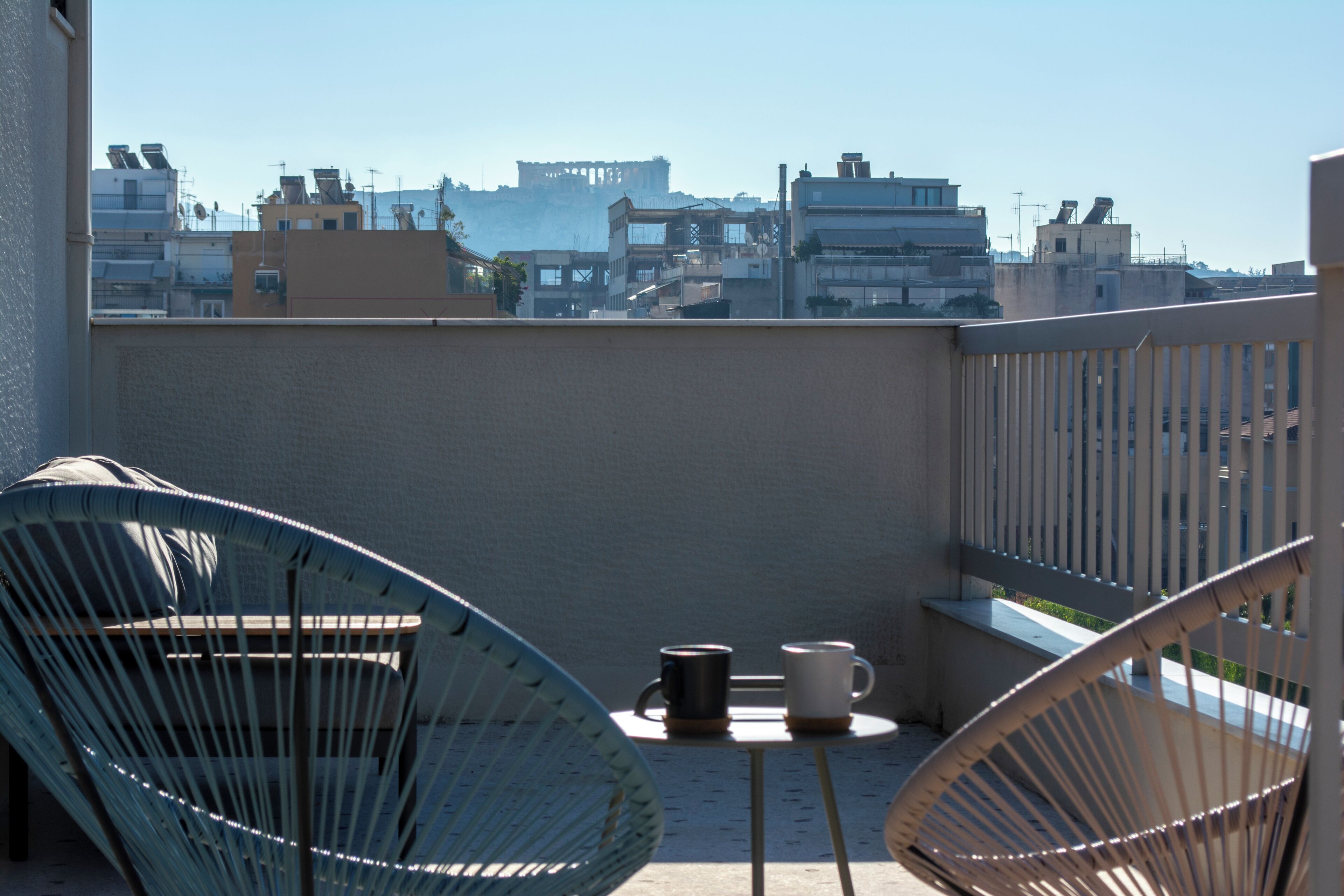 En balkon med to fletstole, et lille bord og to kopper.