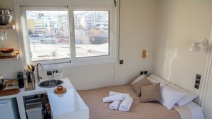 A compact hotel room with a bed, a small kitchenette, a window with a city view, and a bedside table. - Studio with a view of the Acropolis, close to the metro and tourist attractions (Athina)