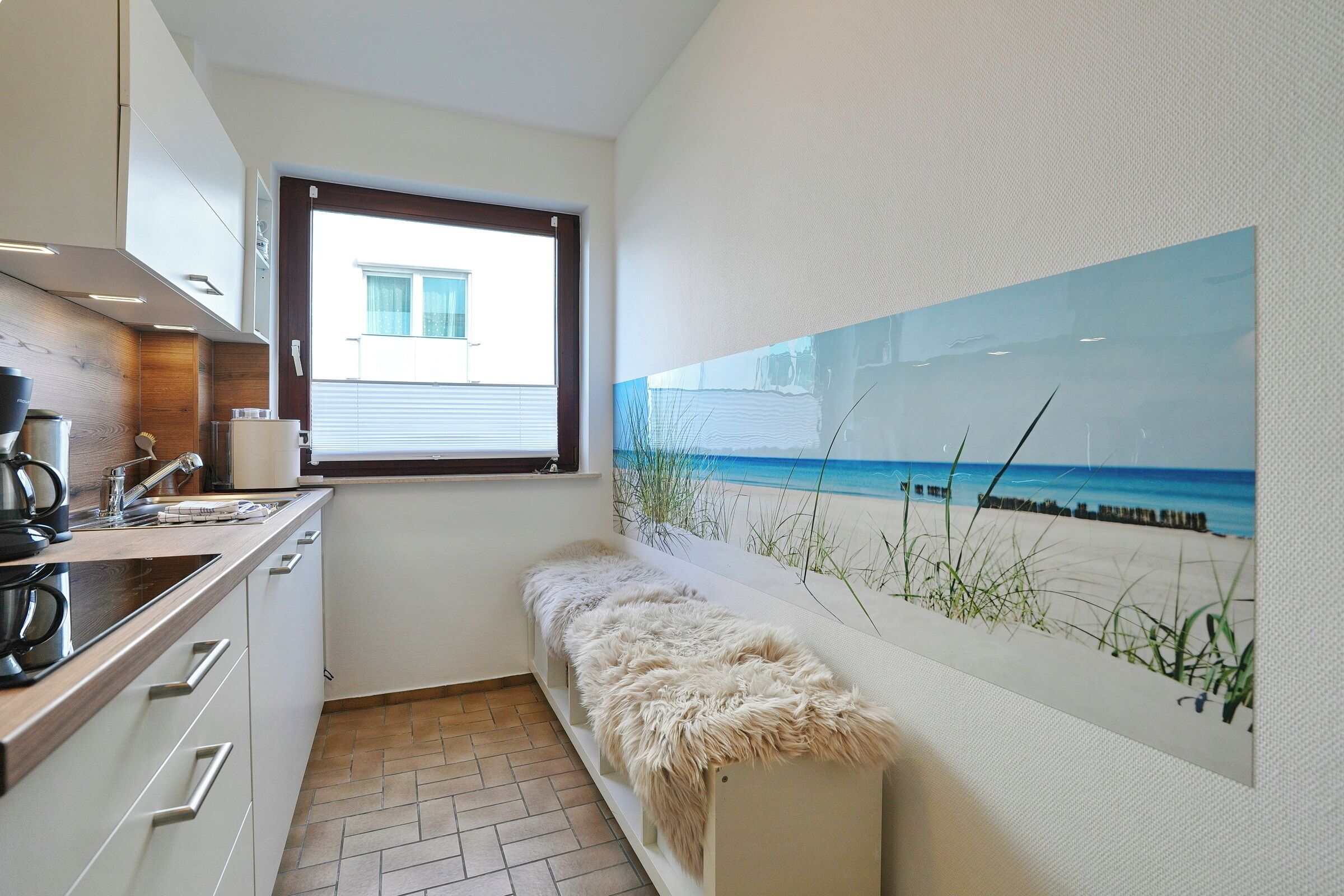 Una cocina con ventana, un cuadro de una playa y un banco de piel.