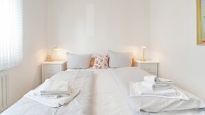 A hotel room with two beds, white bedding, a nightstand with a lamp, and a window with a curtain. - Hansastrasse Building, Apartment 1 (Scharbeutz)