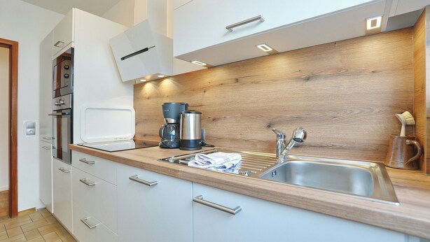 A modern kitchen with a wooden countertop, stainless steel sink, and built-in appliances. - Hansastrasse Building, Apartment 1 (Scharbeutz)