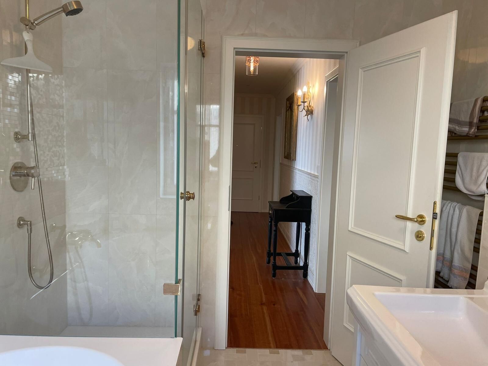 Ein Badezimmer mit einer gläsernen Duschkabine, einer weißen Badewanne und einem Holzboden, der zu einem Flur mit einem schwarzen Klavier führt.