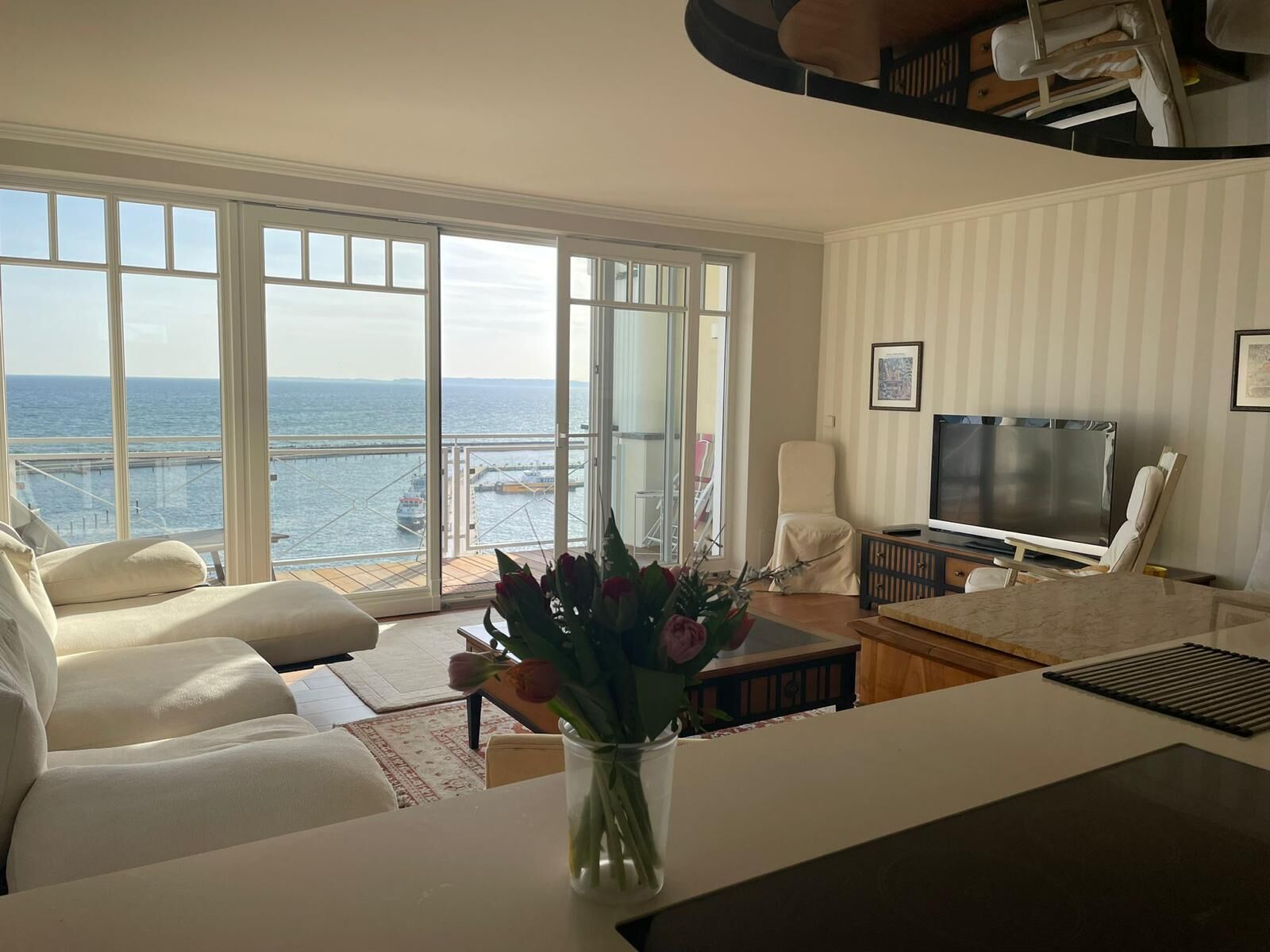 Ein Wohnzimmer mit Meerblick, einem Fernseher und einer Blumenvase.