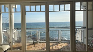 A room with a large sliding glass door leading to a wooden deck with a view of the ocean and a bridge. - "Prinz Heinrich" Ocean View Villa - Molenblick Apartment (Sassnitz)