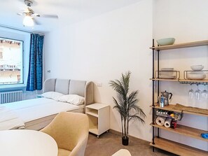A room with a bed, a chair, a plant, a shelf with kitchen items, and a window with curtains. - Via Monte Brione by Interhome (Arco)