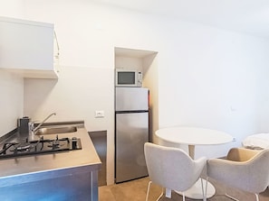 A compact kitchen with a gas stove, sink, and a refrigerator. There is a microwave on top of the fridge, and a small table with two chairs. - Via Monte Brione by Interhome (Arco)
